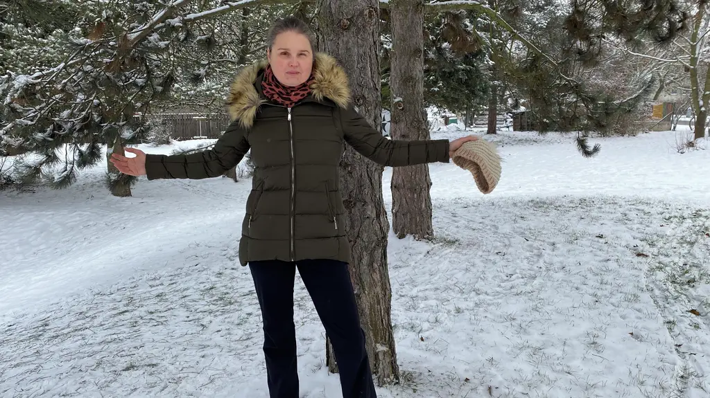 Linda stojí ve sněho před stromem a má rozpažené rucepřed 