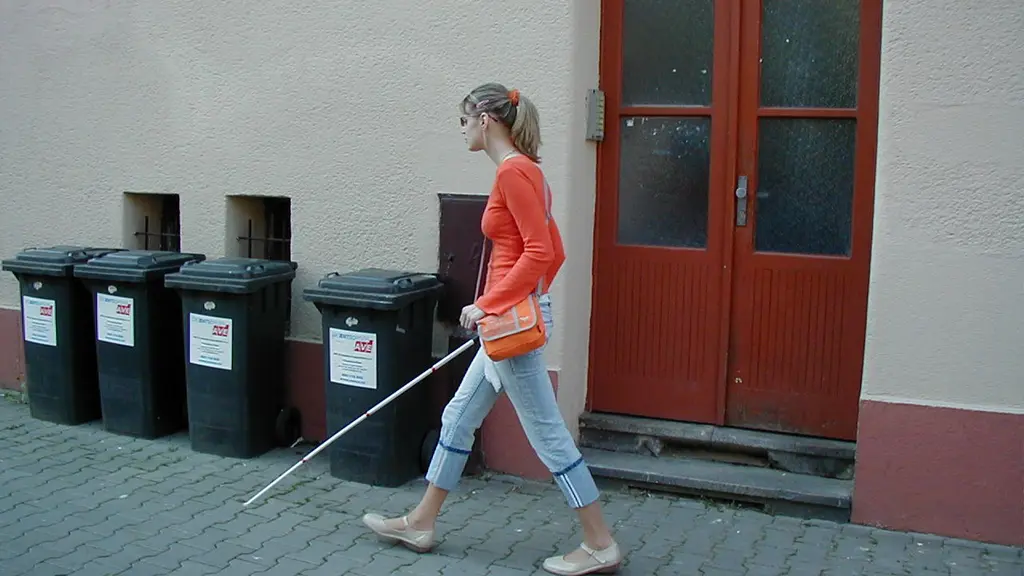 gívka s bílou holí jde okolo kontejnérů