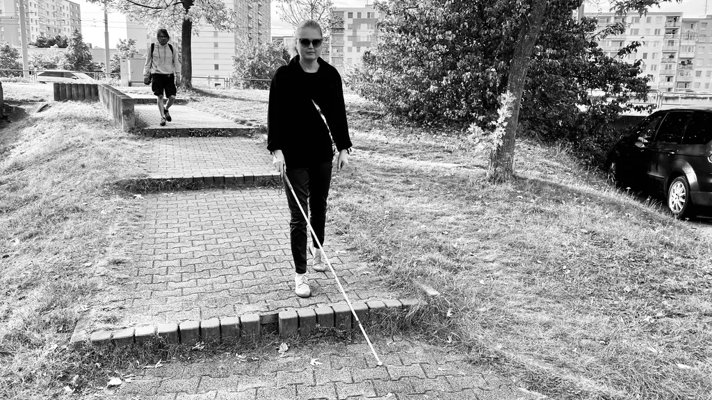 Autorka jde s bílou holí po schodech na chodníku